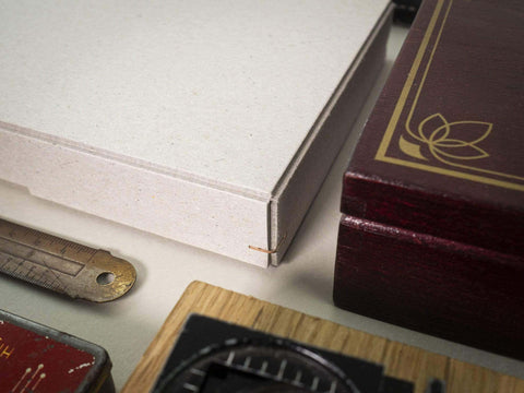Detailansicht einer Ecke einer handgefertigten Design Box aus Graukarton. Format 23cm x 16,5cm x 2,5cm. Die Drahtheftung an jeder Ecke verleiht der Box einen edlen Look. 